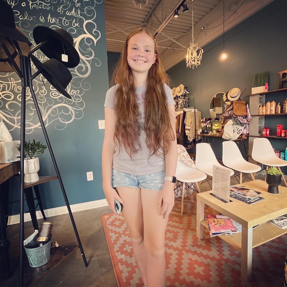 Customer smiling inside the in-salon boutique, surrounded by clothing racks, hats and bags